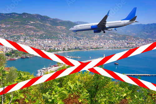 Flight ban. Crossed barrier tapes with red and white stripes against the background of a flying plane.