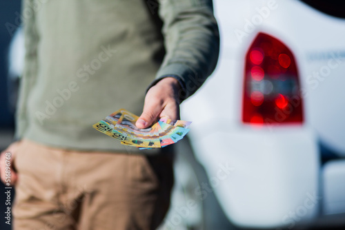 Young man holding cash standing in front of car paying up front