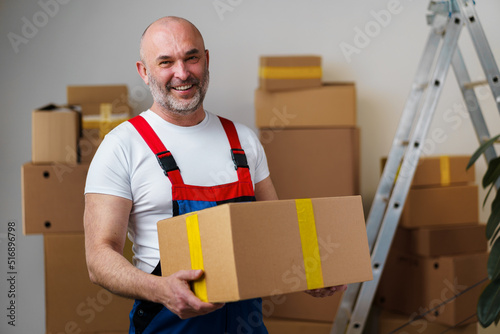 Middle-aged man mover in uniform holding cardboard box, portrait photo