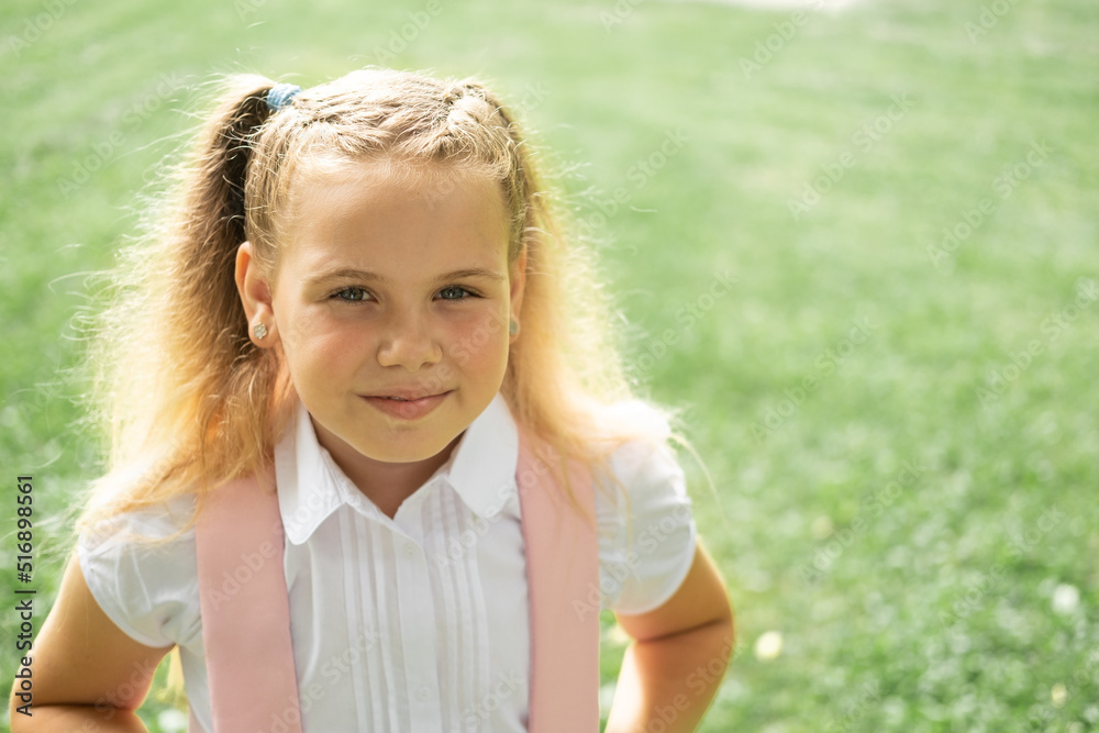 close up portrait of smiling blonde schoolgirl in white shirt with pink backpack back to school outdoor