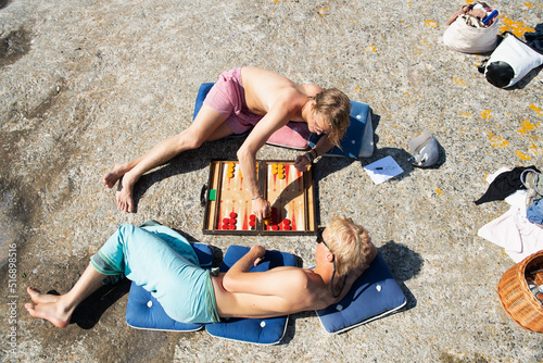 Fotografering Young men lying down playing backgammon on rock
