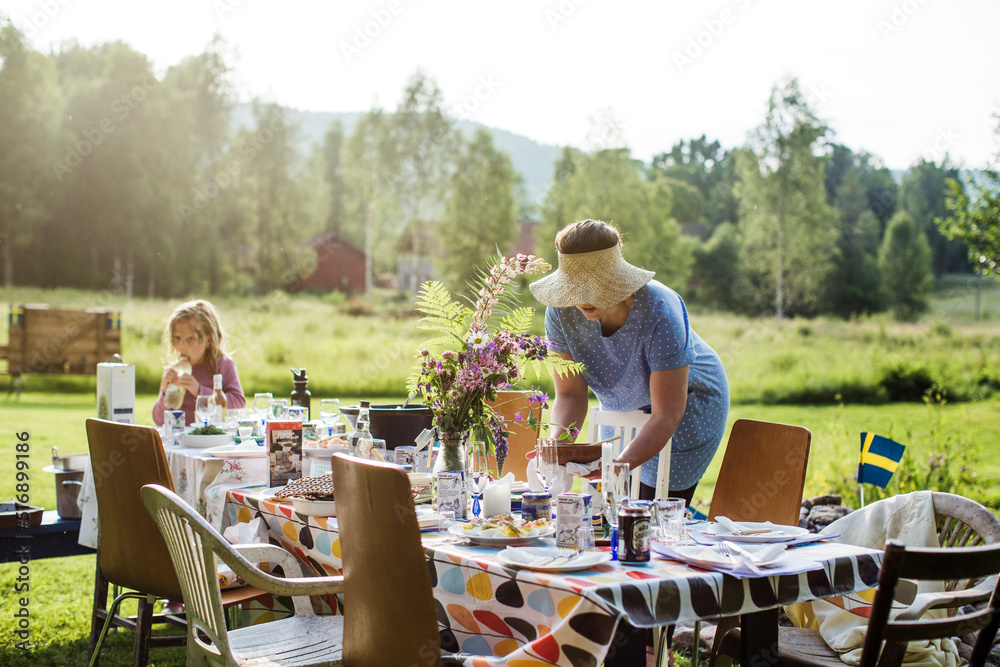 Woman and her daughter setting dining table outdoors Woman and her daughter setting dining table outdoors