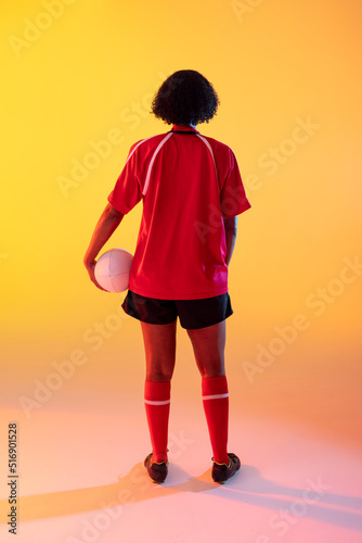 Rear view of african american female rugby player with rugby ball over neon yellow lighting
