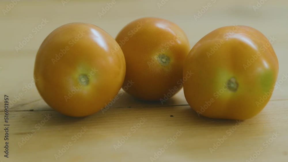 two tomatoes on wooden table, another one comes rolling in two tomatoes on wooden table, another one comes rolling in