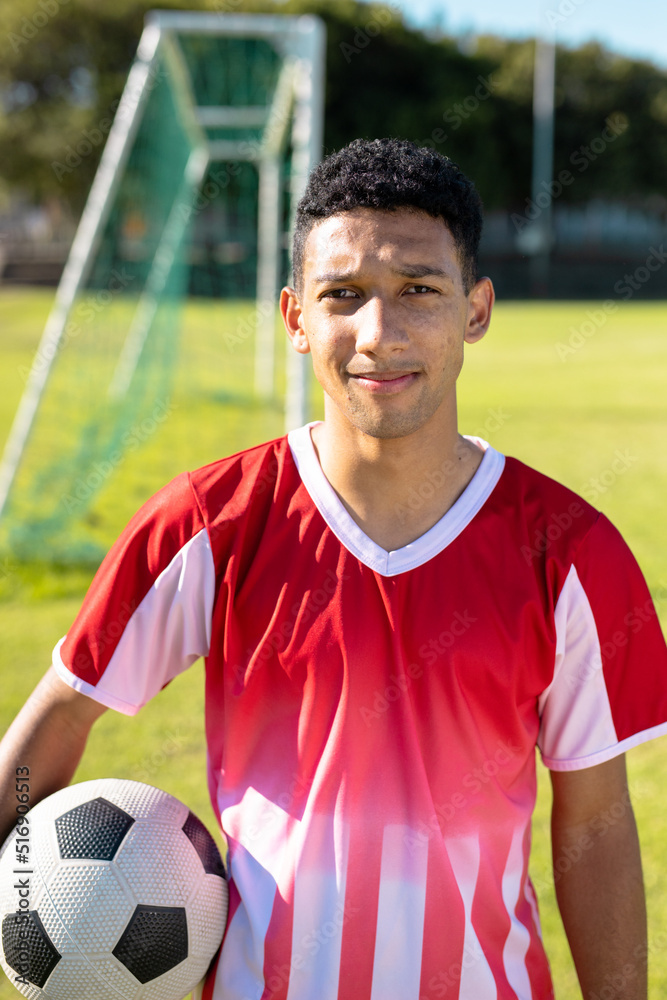 Portrait of confident caucasian young male player in red jersey with ball standing at playground