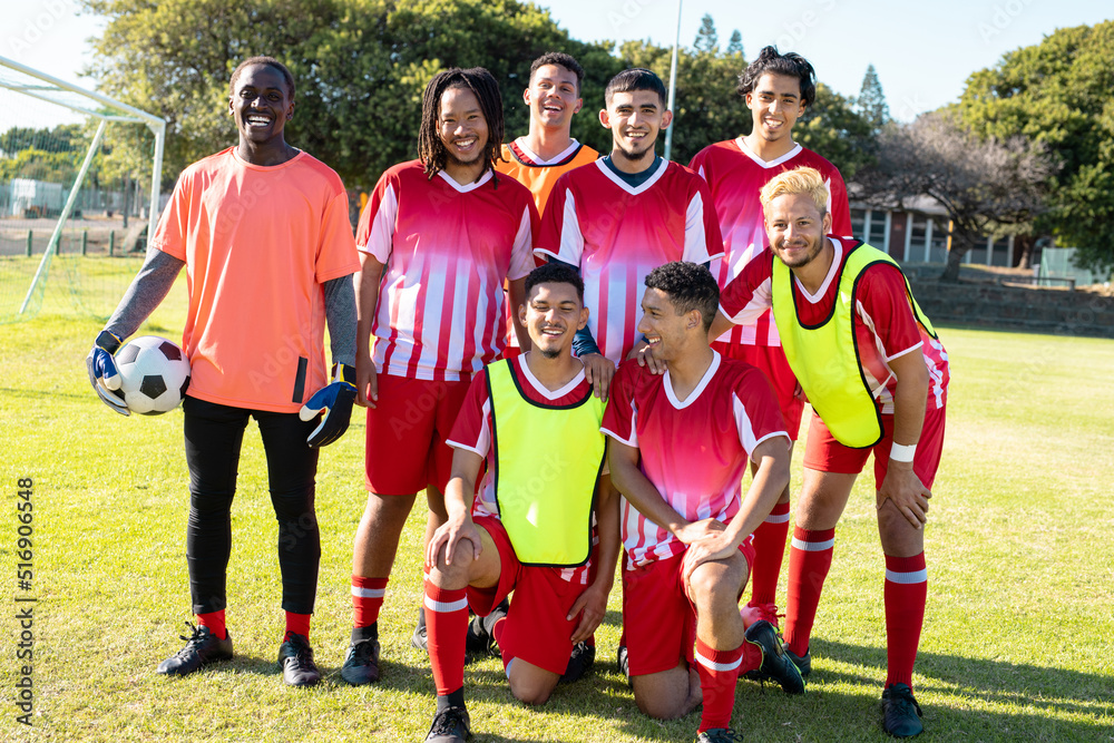 Portrait of happy male soccer team players wearing uniforms posing in playground during sunny day