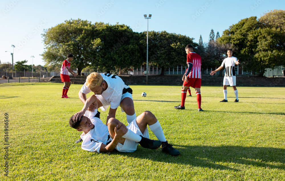 Obraz premium Multiracial male player assisting injured teammate lying on field in getting up during match