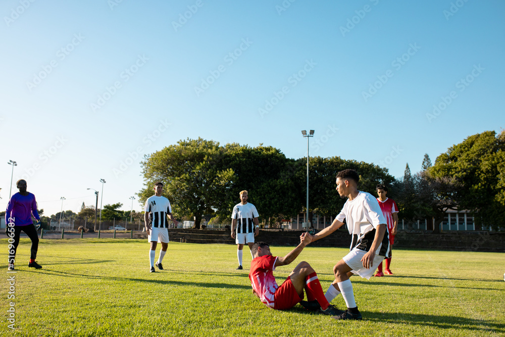 Obraz premium Multiracial player holding hand and assisting injured opponent to get up during match at playground