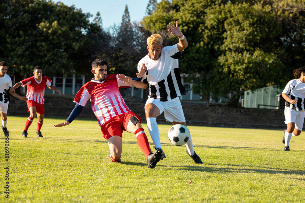 Obraz premium Male multiracial players running and kicking the soccer ball during match at playground in summer