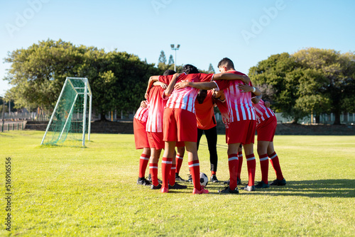 Male multiracial players in red uniform with arms around discussing and huddling at playground