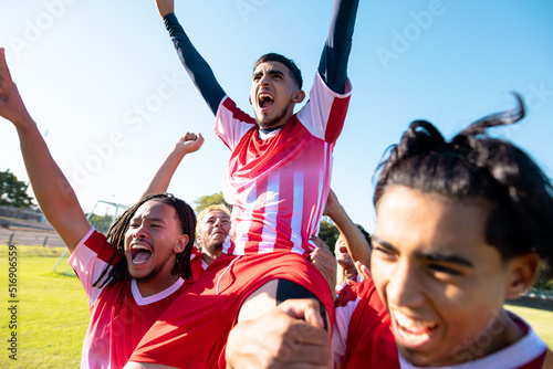 Multiracial male players carrying cheerful teammate on shoulders screaming while celebrating goal