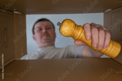 A man pulls a wooden spice mill out of a cardboard moving box. Yellow handmill for peppers, sloe and other spices and condiments. Bottom view. Inside view. Close-up. Selective focus. photo