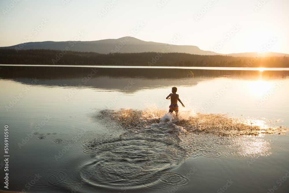 Boy splashing in Ottsjo Lake at sunset in Valadalen Nature Reserve Sweden Boy splashing in Ottsjo Lake at sunset in Valadalen Nature Reserve Sweden