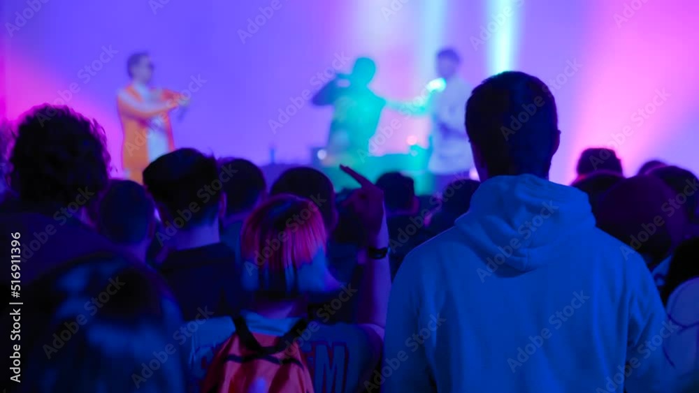 Slow motion: teenagers partying, cheering, raising hands up and jumping at rock concert in front of stage of nightclub. Bright colorful stage lighting. Nightlife and entertainment concept Slow motion: teenagers partying, cheering, raising hands up and jumping at rock concert in front of stage of nightclub. Bright colorful stage lighting. Nightlife and entertainment concept