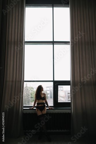 Gorgeous woman wearing black lingerie indoors. Portrait of a beautiful dreamy girl in a black underwear by the window