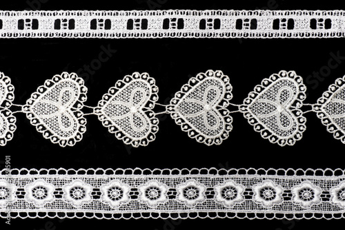 White lace with flowers and hearts and leaves isolated on black background horizontally