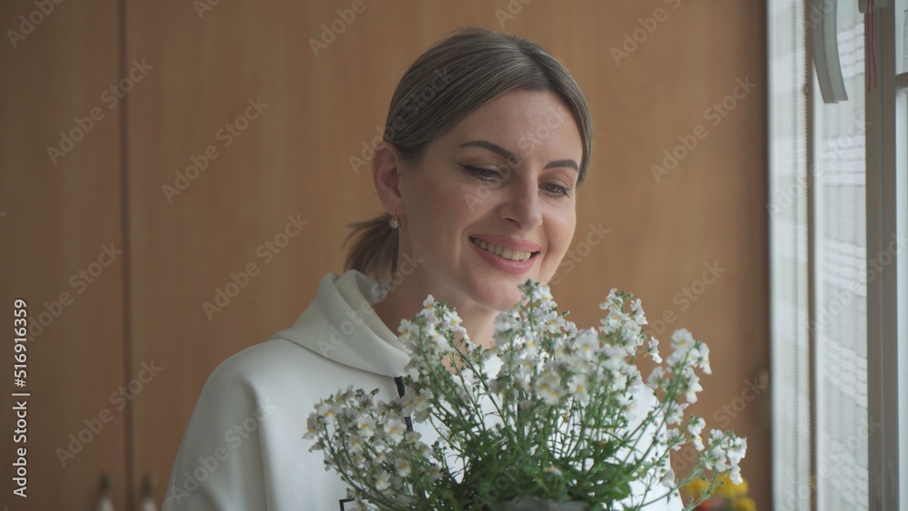 Young woman with bouquet in her hands, looks at flowers and smiles.
