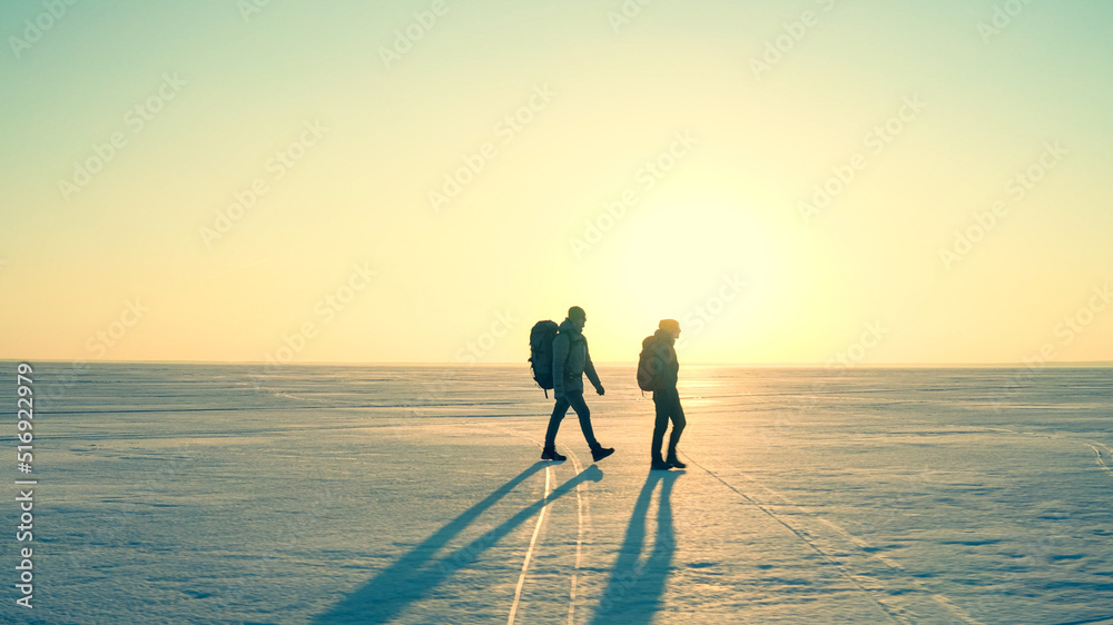 The two travelers with backpacks trekking through the snow field