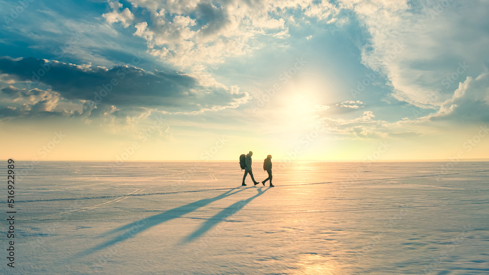 The two travelers with backpacks trekking through the snow field