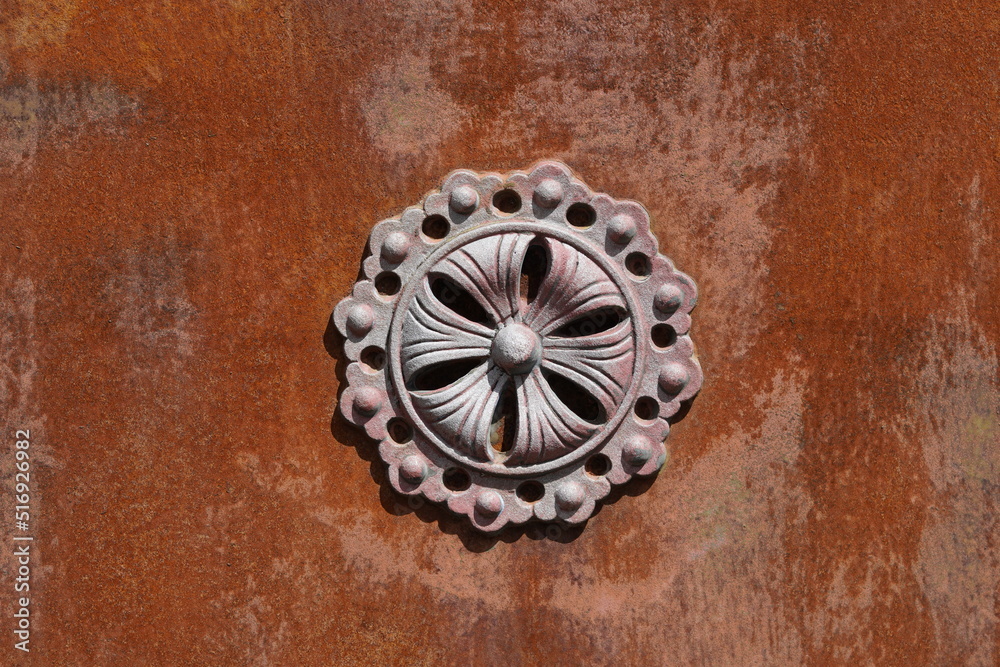 Metallic ornament in the shape of a flower on a rusted background.
