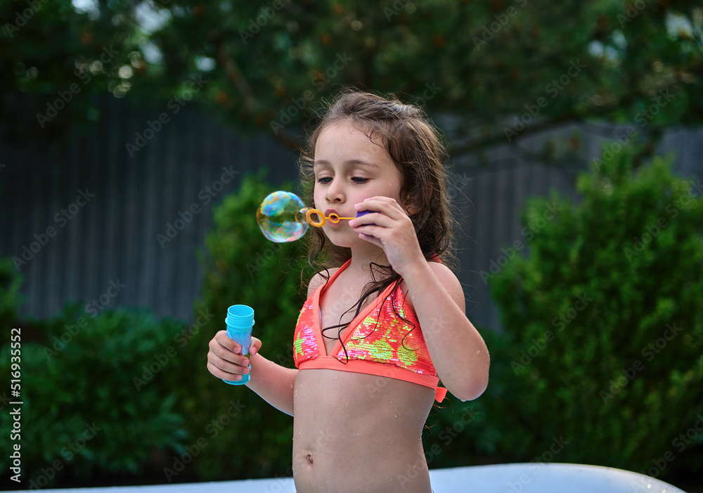 Caucasian funny little girl, blows soap balls in the inflatable water pool on summer vacation. Caucasian funny little girl, blows soap balls in the inflatable water pool on summer vacation.