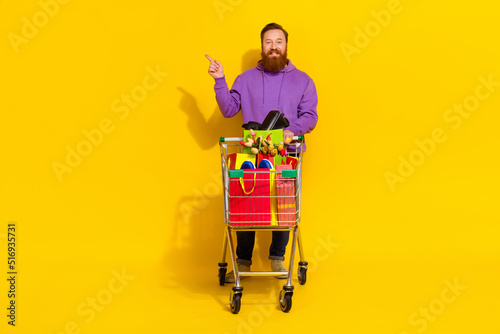 Full body photo of positive young guy indicate finger empty space offer isolated on yellow color background