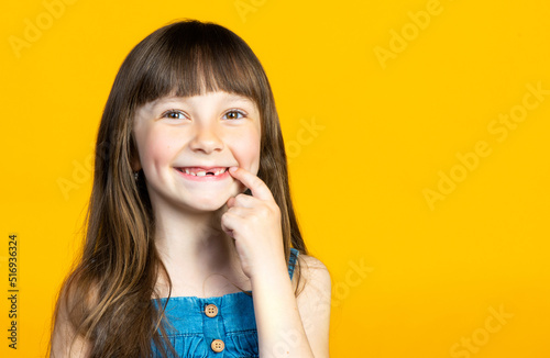 The little girl's front tooth fell out, toothless smile of a first grader. Isolated on yellow background