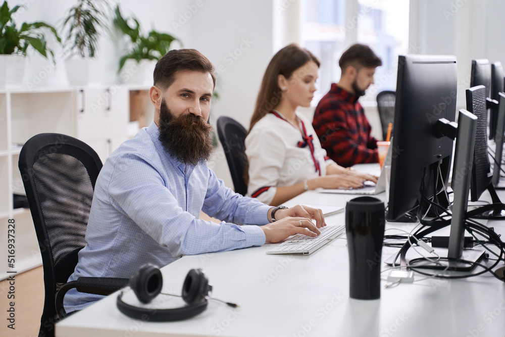 People working in modern IT office. Group of young and experienced programmers and software developers sitting at desks working on computers. Team at work.