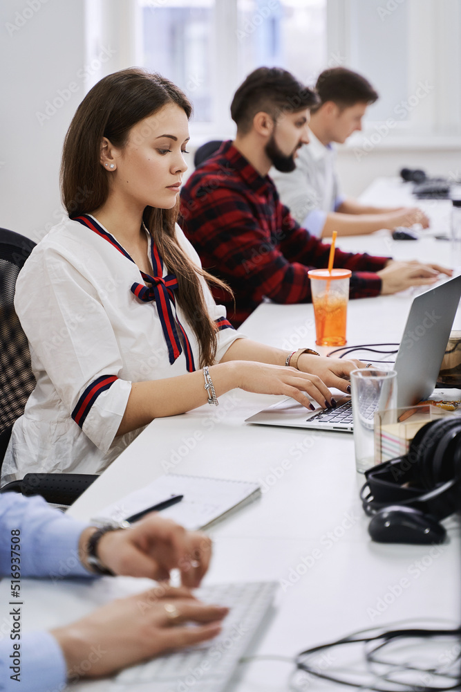 People working in modern IT office. Group of young and experienced programmers and software developers sitting at desks working on computers. Team at work.
