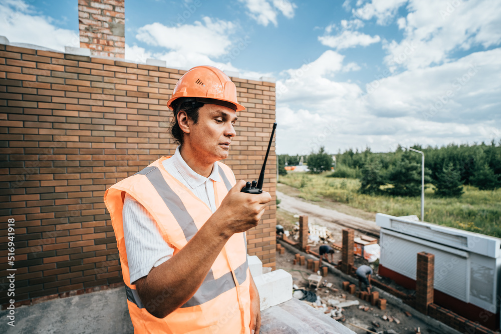 Foreman inspector or construction worker in hardhat portrait. Engineer in helmet with walkie-talkie in hand directs construction process.