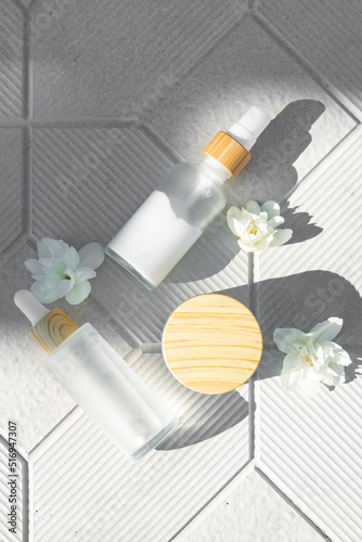 Cream, serum,essence, oil in frosted glass packaging with jasmine flowers. Cosmetic skincare producton on concrete background.Top view