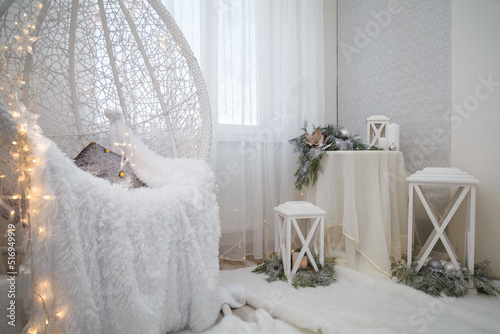 Beautiful white lace cocoon chair with plaid and cushion, golden garland lights in room decorated for Christmas. Magic Christmas vibes photo