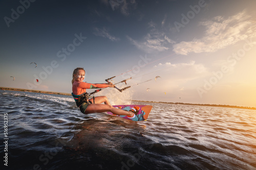 Water sports. The girl is engaged in kitesurfing with a kite in the sky on board in the blue sea, riding the waves with water splashes. Recreational activities,