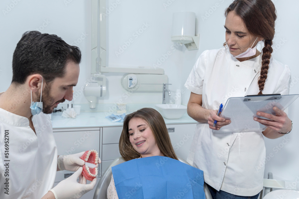 Young man dentist showing dental jaw model to female patient in dentist's office. Young man dentist showing dental jaw model to female patient in dentist's office.