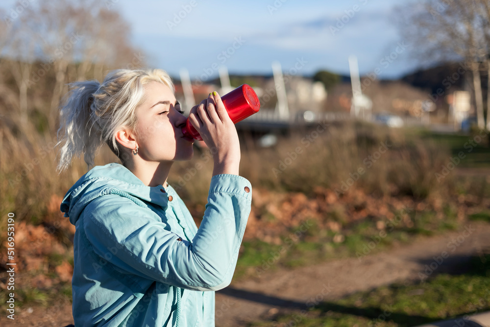 Runner woman drinking water after workout in a public park 