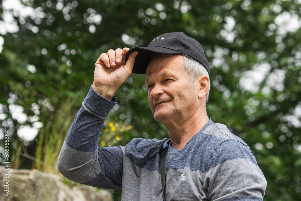 Obraz premium Portrait of smiling caucasian senior man with black baseball cap and casual clothing. Isolated on the nature background.