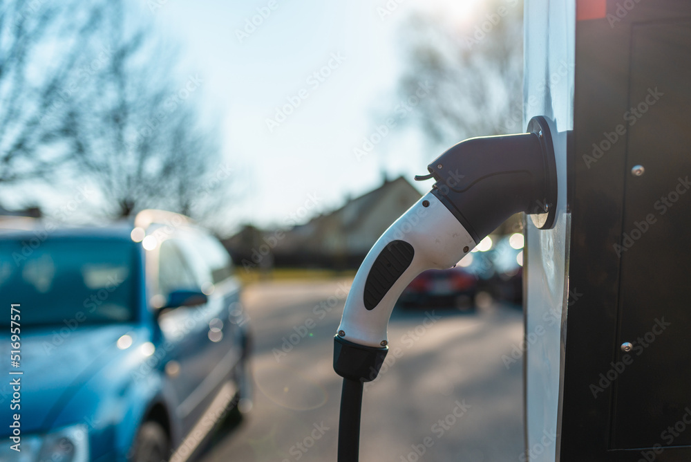 Close up power cord for electric car. Green station.Power supply for electric car battery charging.Blurred car in the background.Selective focus.Closeup. Close up power cord for electric car. Green station.Power supply for electric car battery charging.Blurred car in the background.Selective focus.Closeup.