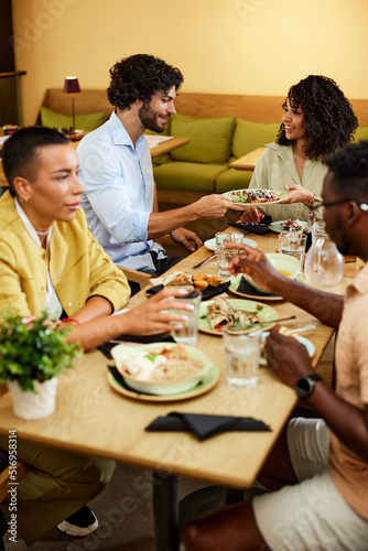 A group of multicultural friends is sitting in a restaurant  chatting and eating lunch on a lunch break.