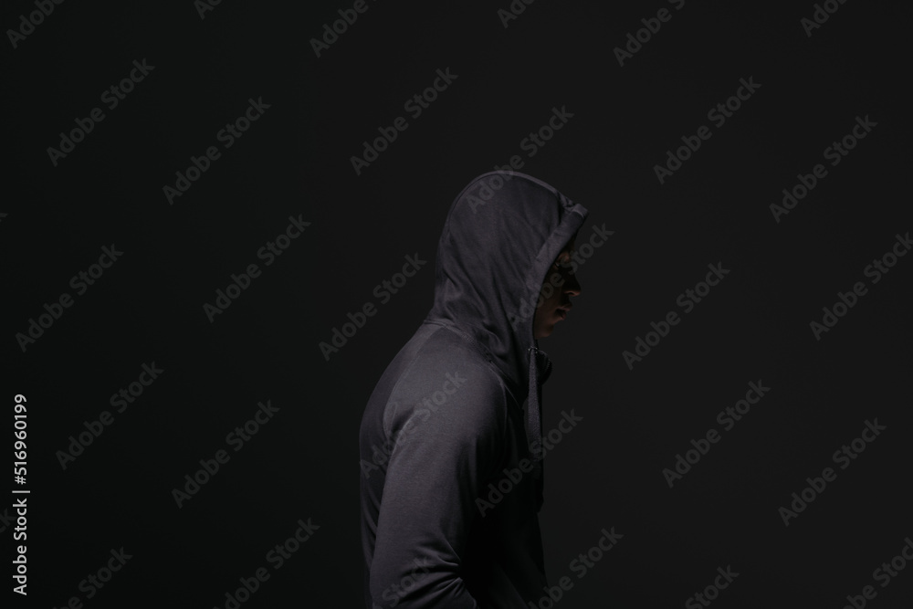 Side view of african american hooligan in hood standing isolated on black - obrazy, fototapety, plakaty 