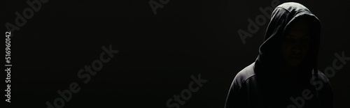 Silhouette of hooligan in hoodie with lighting isolated on black, banner photo