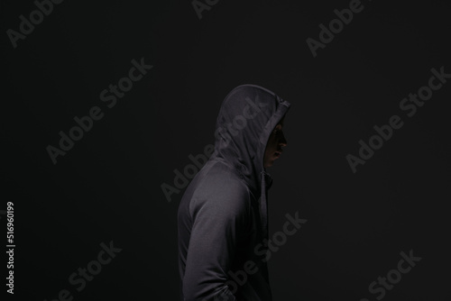 Side view of african american hooligan in hood standing isolated on black