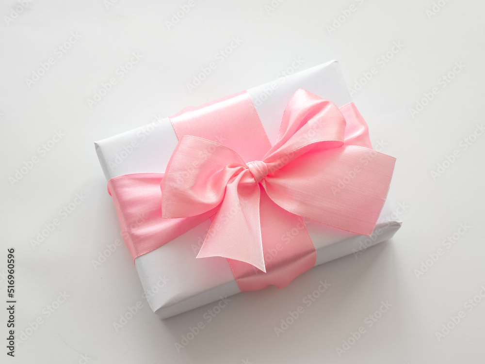 Wrapped gift box with a delicate pink bow, the concept of a holiday on March 8 or Valentine's Day Wrapped gift box with a delicate pink bow, the concept of a holiday on March 8 or Valentine's Day