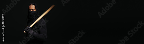 African american hooligan with mask on face holding baseball bat isolated on black, banner