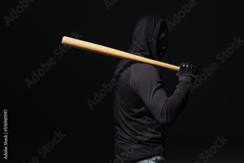 Side view of african american hooligan in mask and glove holding baseball bat isolated on black