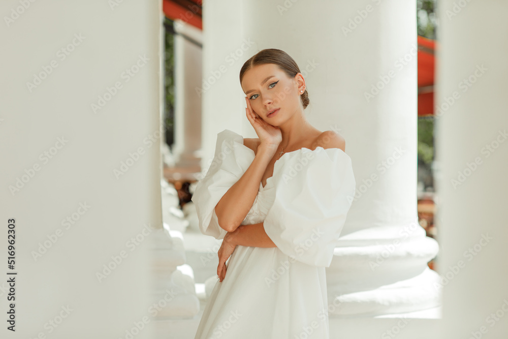 A young beautiful woman in a white dress near the columns A young beautiful woman in a white dress near the columns