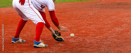 Baseball infielder fielding the ball on a red turf field