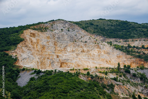 Natural quarry is located near road against backdrop of Rhodope Mountains and hills with forests and mountain vegetation