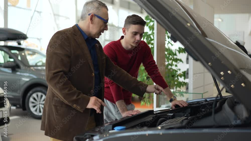Two male visitors are examining new transport and standing in modern company spbd. 4k Closeup view of young son, elderly father study engine of car and talk with smiles, make decision and stand in Two male visitors are examining new transport and standing in modern company spbd. 4k Closeup view of young son, elderly father study engine of car and talk with smiles, make decision and stand in