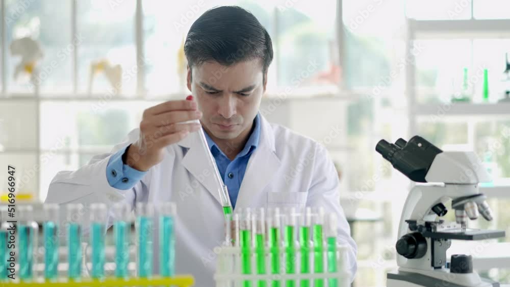 Young male researcher analyzing liquid on microscope at laboratory Young male researcher analyzing liquid on microscope at laboratory