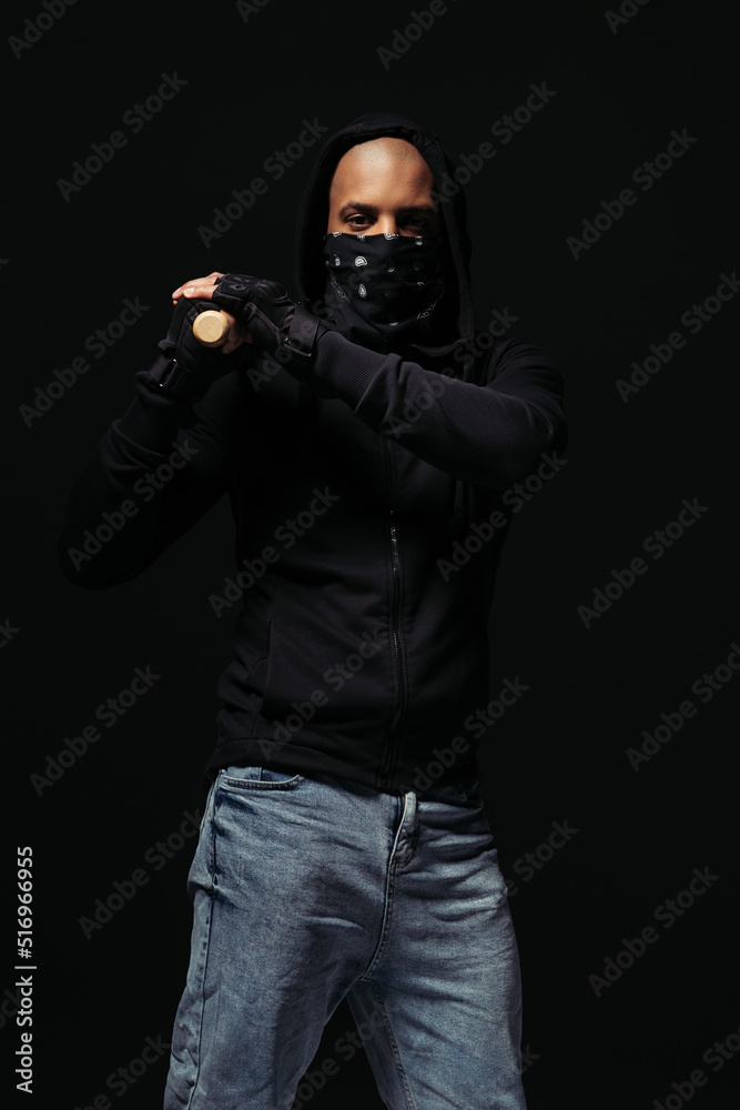 African american hooligan in gloves and face mask holding baseball bat isolated on black